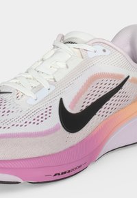 Λευκό παπούτσι Nike για τρέξιμο με μαύρο λογότυπο swoosh, ροζ και πορτοκαλί λεπτομέρειες, λευκά κορδόνια και ροζ σόλα με την ένδειξη "Air Zoom."