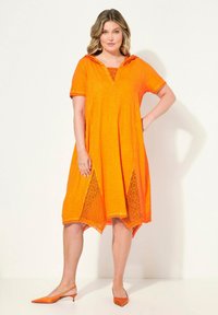 Orangenes Kleid mit kurzen Ärmeln und einer Kapuze. Verfügt über ein Spitzenpaneel an den Seiten. Strukturierter Stoff mit einer leicht lockeren Passform und asymmetrischem Saum.