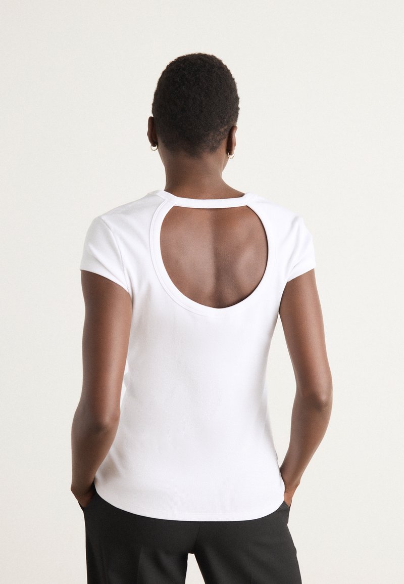 T-shirt blanc ajusté avec une petite découpe ronde au dos, des manches courtes et une texture lisse, conçu pour un ajustement proche et le confort.