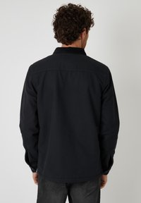 Zwarte jas met een kraag, lange mouwen en knoopmanchetten. Stof lijkt textuur te hebben, met een relaxte pasvorm en eenvoudig ontwerp.