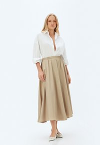 Chemise blanche à boutons avec des manches retroussées et un décolleté profond, associée à une jupe beige mi-longue avec une ceinture élastique.