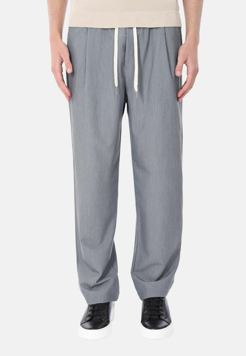 Pantaloni grigi plissettati con vita elastica e cordino. Tessuto liscio. Abbinati a sneakers nere e bianche.