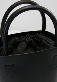 Sac à main en cuir noir avec poignées rondes, présentant une doublure intérieure noire froncée et un design minimaliste. Texture lisse avec des accents subtils.