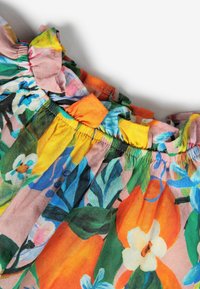 Bunt gemusterter Blumenstoff mit Flatterkragen-Detail. Die Materialien bestehen aus leichtem Textil mit verschiedenen lebhaften Farben und Blattmustern.
