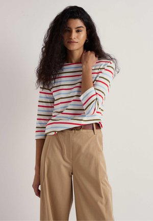 Camicia a righe con linee orizzontali rosse, verdi, blu e bianche, abbinata a pantaloni beige a vita alta. Vestibilità comoda con maniche a tre quarti.