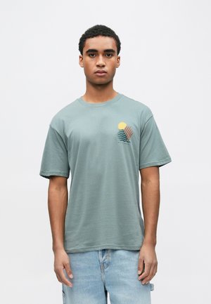 Gray-green short-sleeve t-shirt with a round neck and a graphic of sun and waves in orange and yellow on the left chest area.