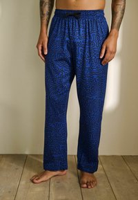 Zila rakstaina pidžamu bikses ar aukliņu jostasvietā, kā arī gluda auduma un abstraktām melnā līniju dizainiem. Brīva piegriezuma, pilnas garuma.