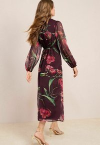 Läpinäkyvä burgundinpunainen maksimekko, jossa on kukkakuosi, joustava vyötärö ja pitkät puffihihat. Mekko on slim-fit-mallia ja sen kangas liikkuu kauniisti.