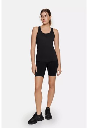 Top atletico nero senza maniche con scollatura rotonda, abbinato a pantaloni da ciclismo neri. Presenta una texture liscia e un design minimalista. Sneakers nere completano l'outfit.