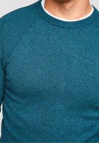 Maglione lavorato a maglia color verde smeraldo con scollo rotondo, maniche raglan e motivo strutturato sulle spalle, realizzato in un tessuto morbido e confortevole.