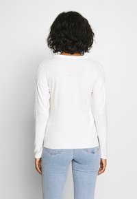 White knitted sweater featuring a textured pattern, ribbed cuffs and hem, and a classic crew neckline, paired with light blue jeans.