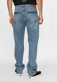 Lyseblå denimjeans med rett benpassform, utstyrt med doble baklommer og et brunt lærbelte som dekorasjon. Svarte sneakers fullfører antrekket.