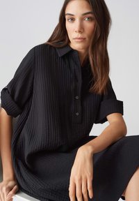 Abito nero con bottoni, caratterizzato da un motivo testurizzato, maniche corte arrotolate e una vestibilità ampia, che arriva a metà polpaccio. Design minimalista.