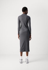 Sivá pletená šaty s dlhým rukávom, s priliehavým strihom a detailom švu na chrbte. V kombinácii s bielymi ponožkami a čiernymi teniskami.