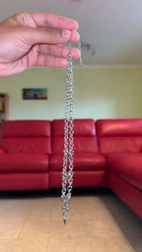 Silverfärgad metallkedja med avlånga länkar, avslutande i en spets; blank yta, varierande storlek på länkar och slät textur.