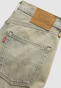 Ανοιχτό μπλε τζιν Levi's που δείχνει πίσω τσέπη με κίτρινο ράψιμο και καφέ δερμάτινη ετικέτα Levi Strauss & Co. στη μέση.