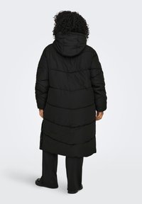 Musta untuvatakki, jossa on huppu, pitkä malli, pystysuorat tikkauskuviot ja piilotetut sivutaskut. Pintamateriaali näyttää sileältä ja eristetyltä.