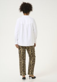 Chemise blanche ample avec un détail au dos, associée à un pantalon imprimé léopard dans des tons beige et noir, présentant une coupe droite.