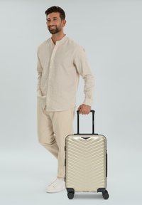 Hartschalenkoffer in metallischem Gold mit Chevron-Muster, schwarzen Akzenten, einem ausziehbaren Griff und vier Rädern für Mobilität.