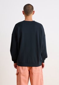 Mörkblå oversized sweatshirt med rund halsringning och sänkta axlar, med ribbade ärmslut och nederkant, bärs med persikofärgade cargobyxor.