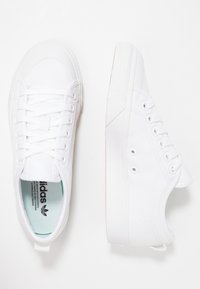 Vita canvas-sneakers med flat sula, rund tå och sex öljetter. Minimalistisk design med texturerad ovandel och diskret märkning på insidan.