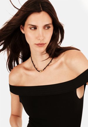 Top negro escotado con banda texturizada. La modelo lleva un collar de cuentas negras con un detalle dorado. Tela suave.