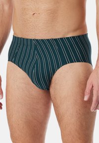 Slip verde a righe con un design aderente, cintura elastica e sottili righe bianche su un tessuto testurizzato. Progettato per comfort e supporto.