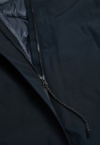 Close-up van een zwarte jack-rits met een zwart-wit trekkoord, gedeeltelijk geopend en de gladde binnenvoering zichtbaar.