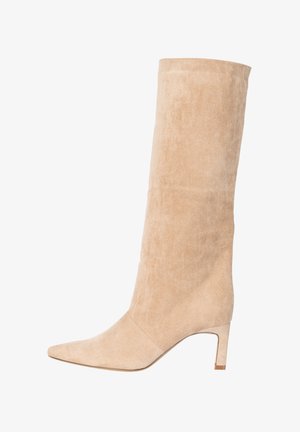 Botte pour femmes en daim beige montant jusqu'au genou, avec un bout pointu et un talon bloc de hauteur moyenne, vue de profil sur fond blanc.