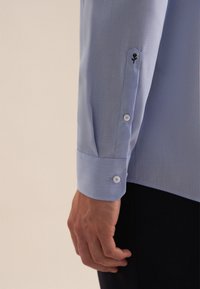 Camicia azzurra chiara con un motivo a righe sottili, dotata di polsini con bottoni blu e un dettaglio di ricamo floreale sulla manica.