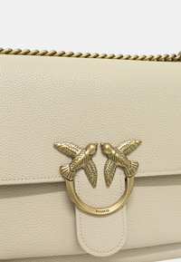 Borsa a tracolla in pelle bianca martellata con fibbia dorata impreziosita da due accenti a forma di uccello e una tracolla a catena.