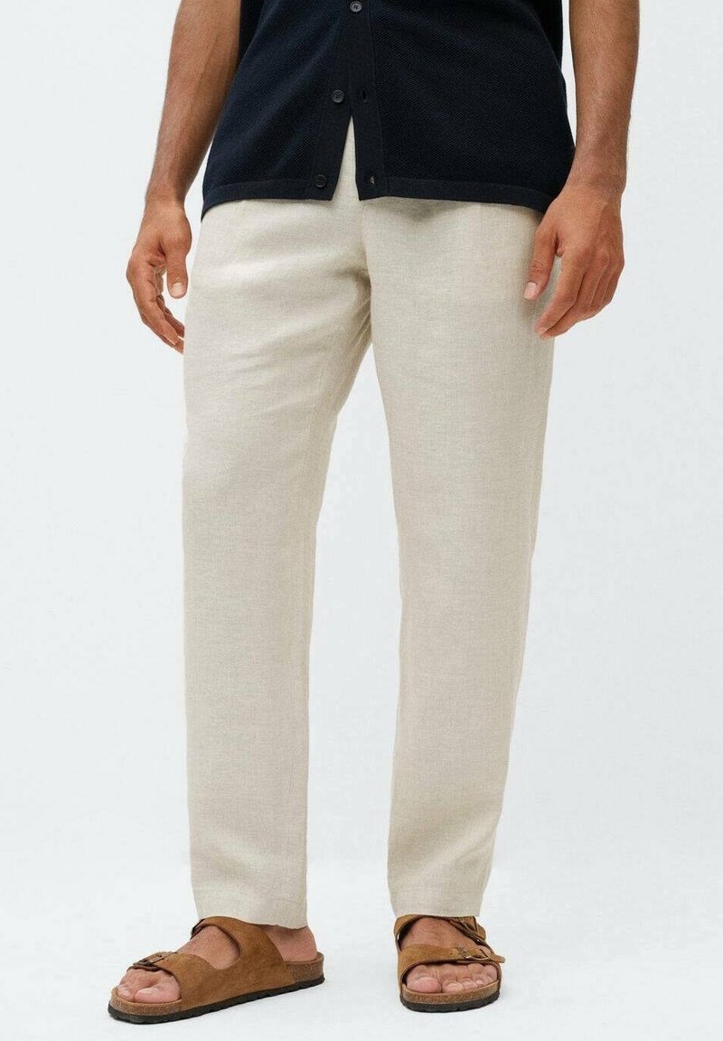 Lichtbeige linnen broek met een recht model en een gladde textuur; gecombineerd met bruine schuifsandalen.
