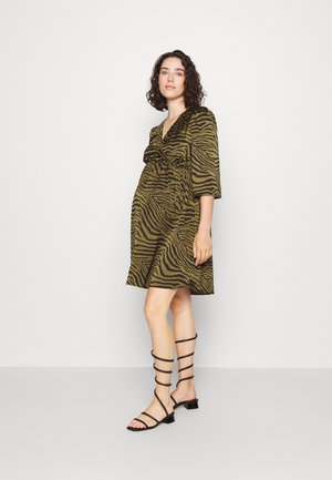 Robe à motif zèbre vert et noir avec un décolleté en V froncé et des manches trois-quarts, associée à des sandales plates noires à lanières.