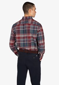 Camisa de cuadros roja y azul de botones con mangas largas, cuello y corte recto. Combinada con pantalones azul marino oscuros y un cinturón marrón.