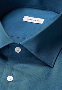 Overhemd met knopen in gestructureerde donkergroene stof. Beschikt over een klassieke kraag, witte knopen en een label met de tekst "seidensticker."