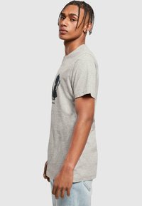Graues Baumwoll-T-Shirt mit Rundhalsausschnitt, kurzen Ärmeln und einem schwarzen Grafikdruck auf der Vorderseite. Getragen mit hellblauen Denimjeans.