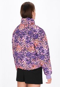 Péřová bunda s výrazným leopardím potiskem v purpurové, růžové a oranžové barvě, s vysokým límcem a elastickými manžetami. Hladká, polstrovaná textura.