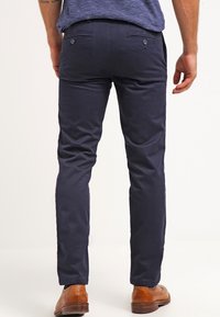 Námořnické modré kalhoty z bavlněného směsového materiálu s úzkým střihem, s kapsami na zadní straně se zapínáním na knoflíky, doplněné hnědými koženými botami.