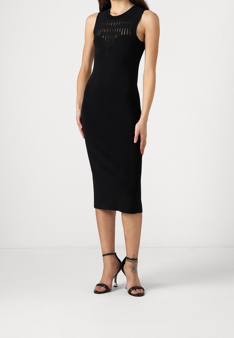 Abito midi nero con design senza maniche, caratterizzato da un sovrapposto testurizzato sul corpino e una silhouette aderente. Accentato da tacchi a strappo neri.