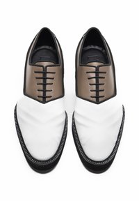 Bicolor leren schoenen met een witte voorkant en een bruine achterkant, zwarte veters, een gestructureerd oppervlak en contrasterende stiksels.