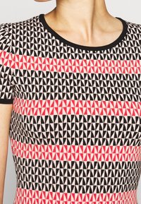 Top à manches courtes en tricot avec un motif géométrique de triangles noirs, roses et rouges, doté d'un col côtelé noir.