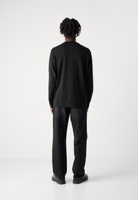 Zwarte lange mouwen shirt met een ronde hals, gecombineerd met zwarte wijde broek. Minimale branding op de achterkant. Glad textuur van de stof.