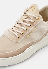 Baskets en daim beige avec lacets blancs, œillets dorés, logo embossé sur le côté et semelle blanche rembourrée.