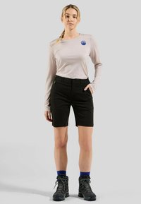 Gaiši bēšas krāsas ar garām piedurknēm krekls ar zilu logotipu, kopā ar melniem šortiem. Melni pārgājienu zābaki ar pelēkām šņorēm papildina apģērbu.