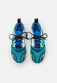 Modré a tyrkysové sportovní boty s texturovaným povrchem, černými tkaničkami, zelenými akcenty a zakřiveným designem. Bílá mezipodrážka s černými detaily.