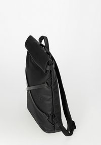 Schwarzer schlanker Rucksack mit aufgerolltem Oberteil, verstellbaren Riemen und prägnantem "alu"-Logo auf der Vorderseite, steht aufrecht vor weißem Hintergrund.