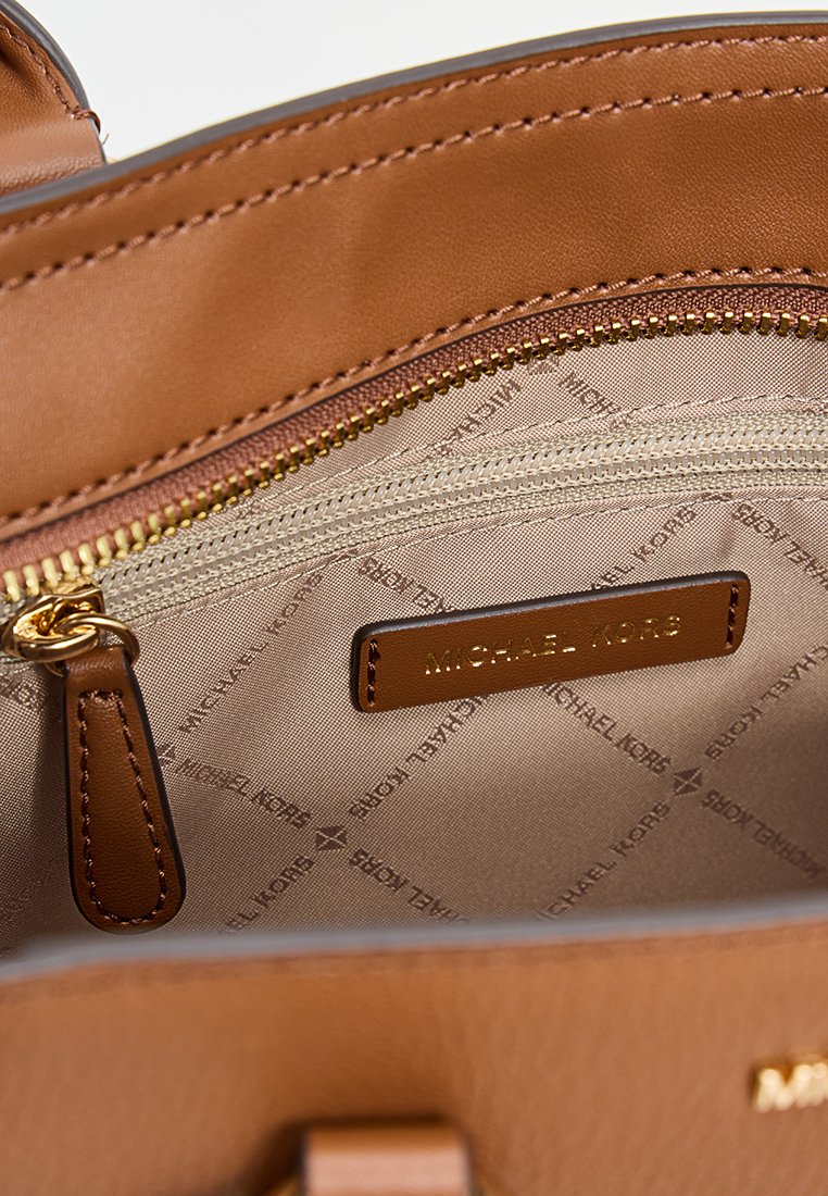 Interior de un bolso de cuero marrón con un bolsillo con cremallera en tono dorado y una etiqueta con el logo de Michael Kors. Forro con un patrón en suave beige.