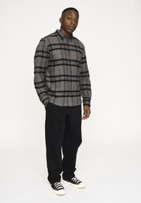 Camicia a quadri grigia con righe nere e grigie; abbinata a pantaloni neri e sneakers nere. Tessuto liscio, design classico.