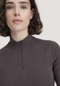 Dunkelgrauer gerippter Pullover mit hohem Kragen und halbem Reißverschluss. Enganliegendes Design, strukturierter Stoff und Raglanärmel betonen den modernen Look.