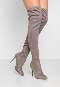 Botas grises de ante por encima de la rodilla, con punta afilada y un alto tacón de aguja. Incluyen una cremallera lateral para el cierre.